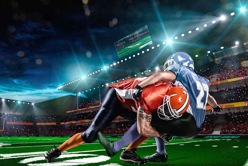 Two football players colliding on the football field against a backdrop of crowded stands and bright lights