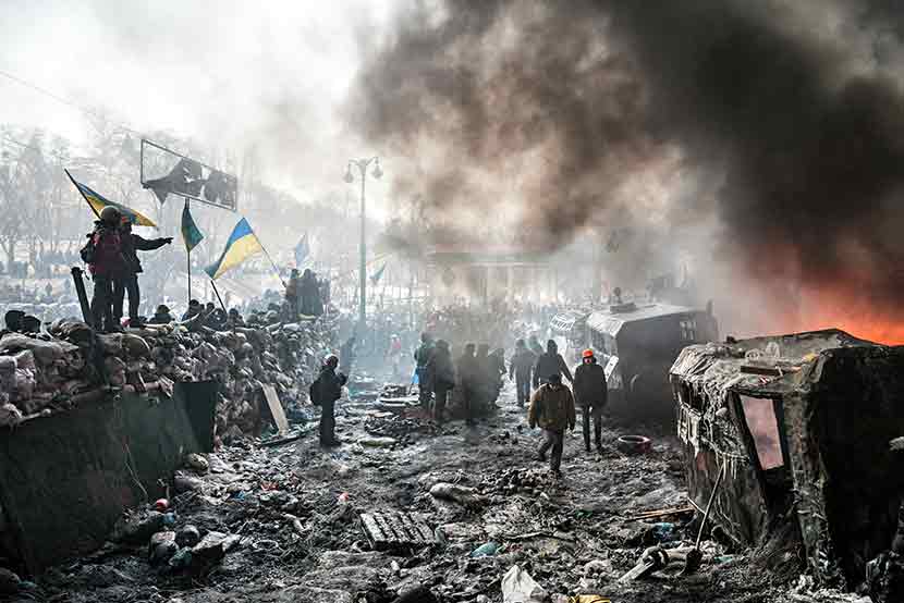The smoking streets of a war torn Ukraine, citizens and militants walking around in the rubble