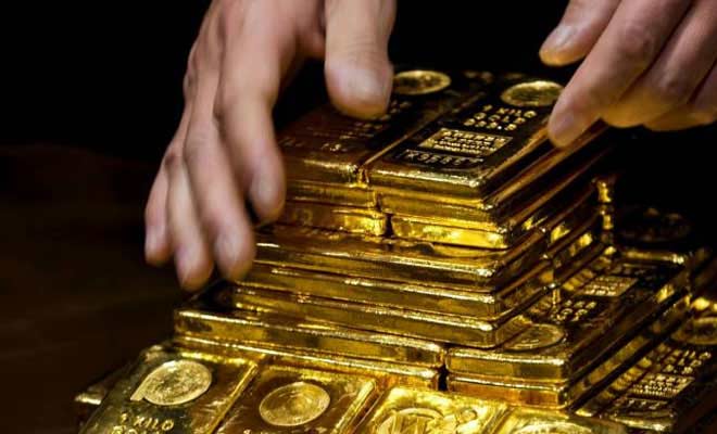 Hands carefully stacking several one kilo gold bars
