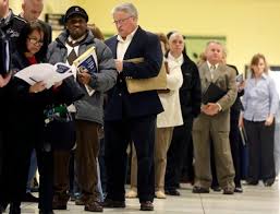 Several unemployed people standing in a line in a room with yellow walls