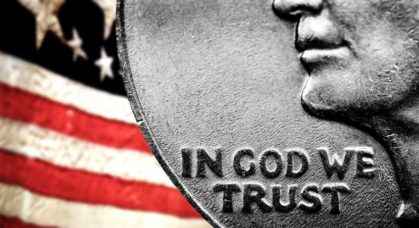 Magnified words on U.S. quarter, In God We Trust, against backdrop of American flag