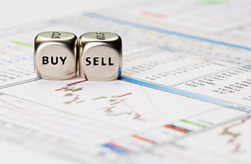 Two silver dice atop stock market reports. One reads "Buy" and the other reads "Sell."