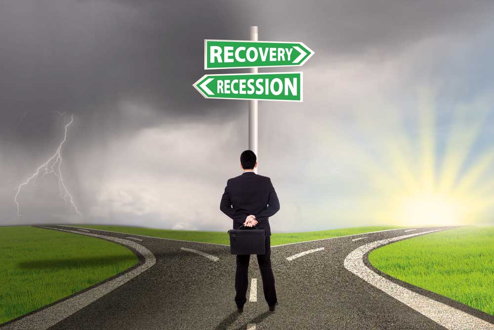 Businessman standing at crossroads of recovery and recession. Recovery points to a cheerful sunrise, while recession points to a dark thunderstorm.