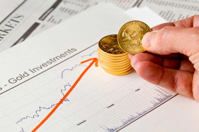 Man holding gold coins and looking at gold investments report with red arrow indicating gold gaining as stocks rout