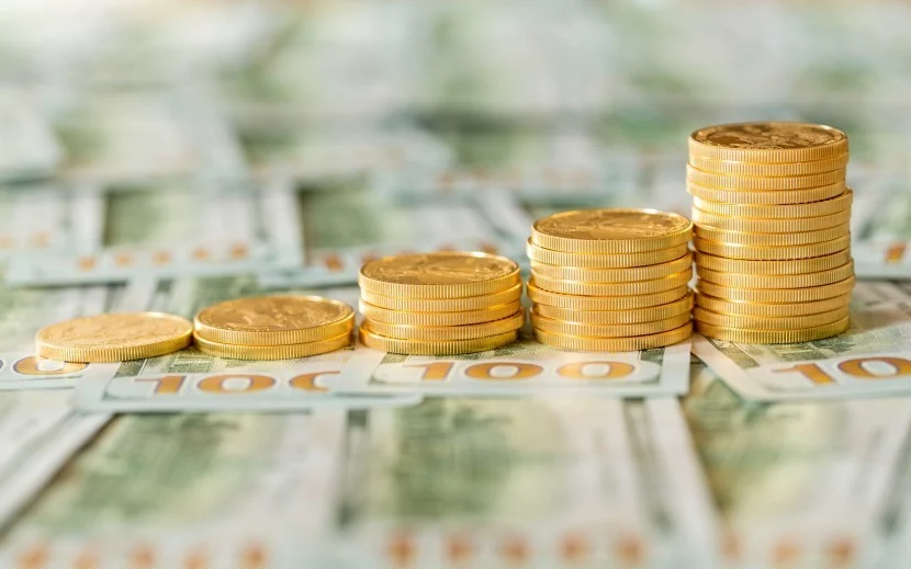 Stacks of gold coins on foundation of one hundred dollar bills, indicating gold prices hit four week high