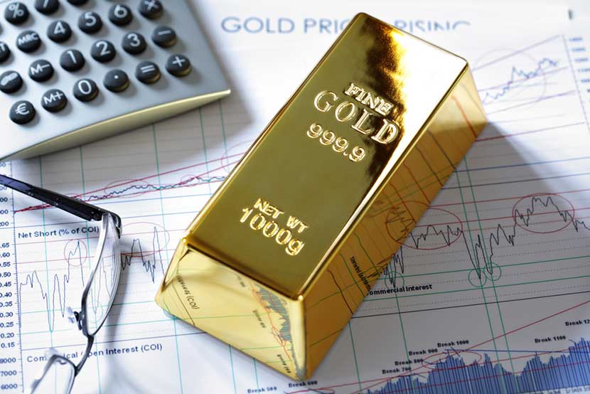 Fine gold bar sitting on stock market reports with calculator