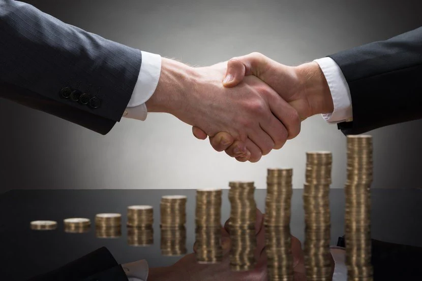 Two business men shaking hands over stacks of gold coins