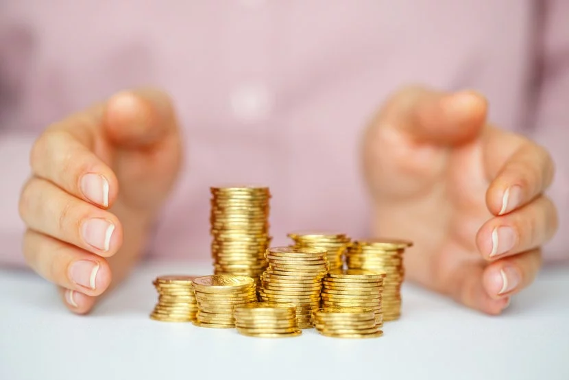 Woman in pink shirt with hands protecting pile of gold coins