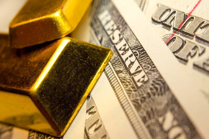 gold-bars-cash-dollars Two gold bars overlaid on top of U.S. currency, close up view of "Reserve"