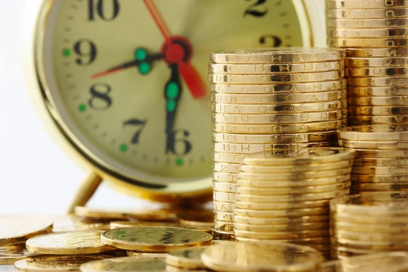 Old fashioned clock in background with stacks of gold bullion coins in the foreground