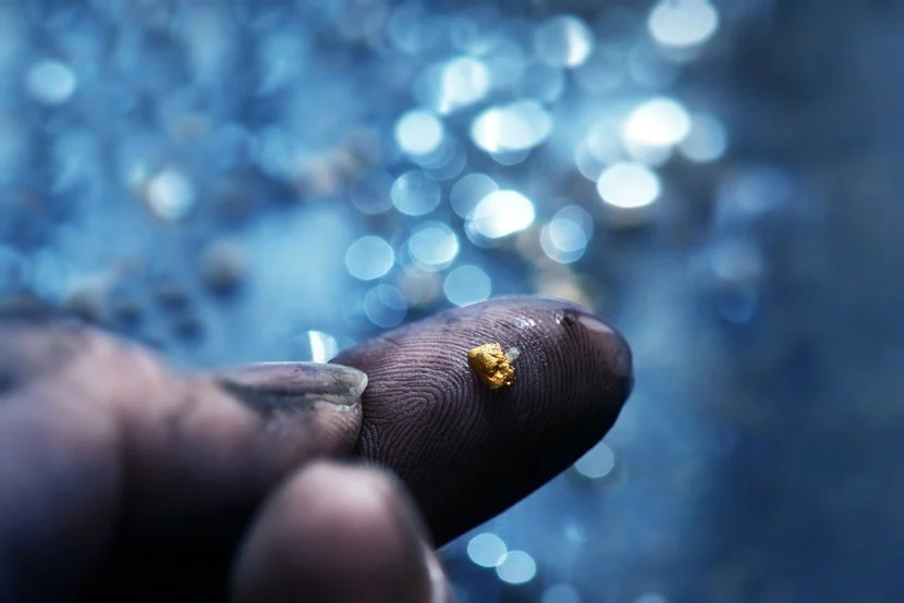 Tiny nugget of freshly mined gold on dirty pointer finger