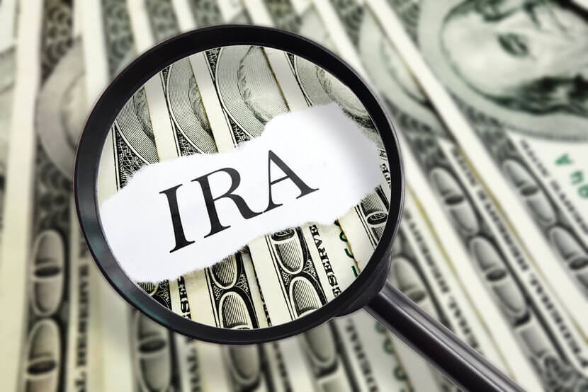 Magnifying glass hovering over IRA on top of U.S. dollars