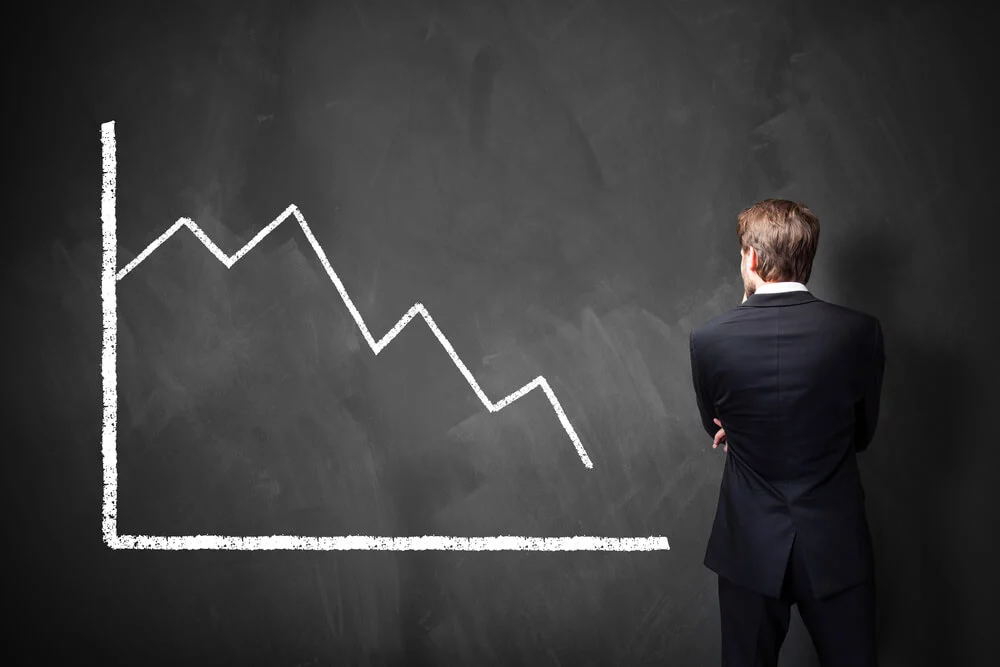 Business man looking at a blackboard with chalk graph showing downward trend