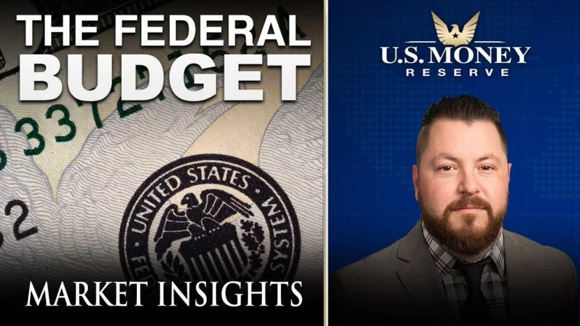 patrick brunson presenting next to an enlarged dollar bill regarding the federal budget