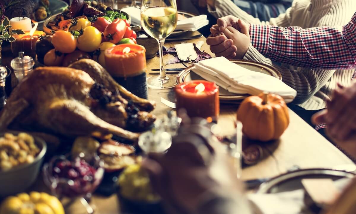 Thanksgiving table with abundance of food on it and people holding hands