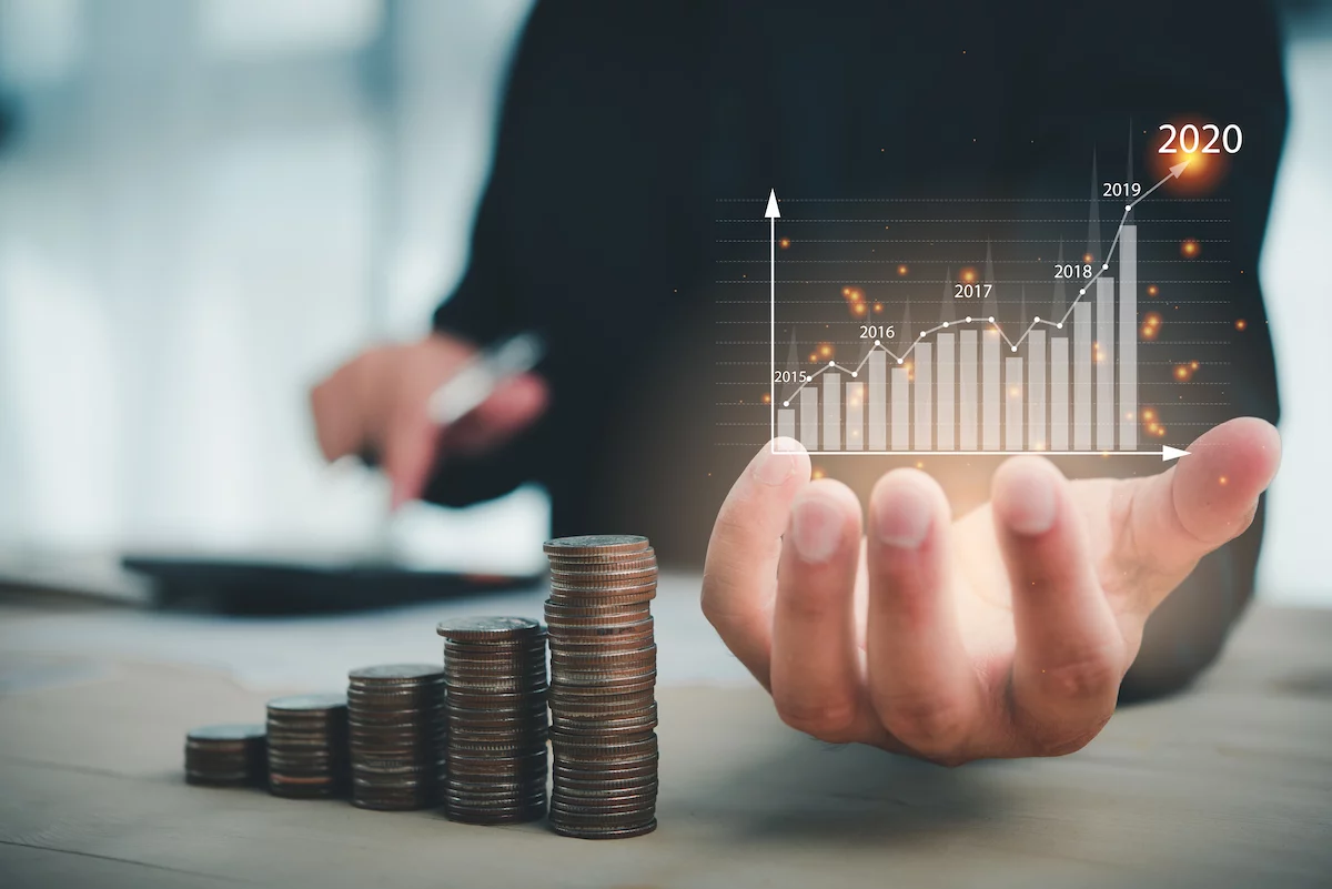Hand holding up projected graph next to stacks of gold coins