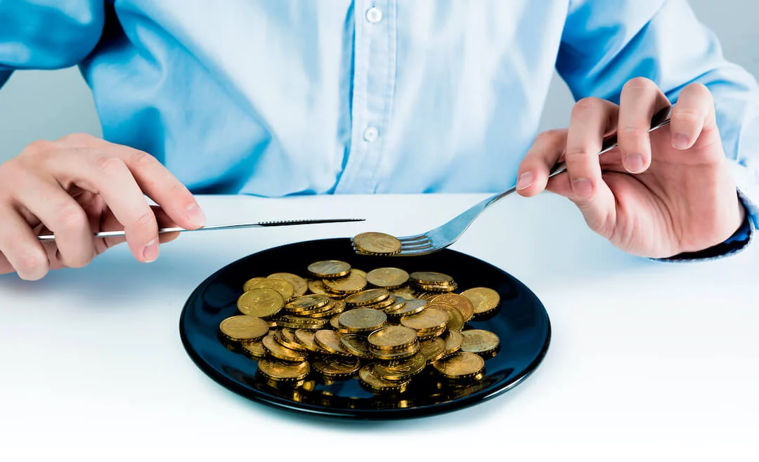 Man with knife and fork holding a cold coin from a plate with gold coins