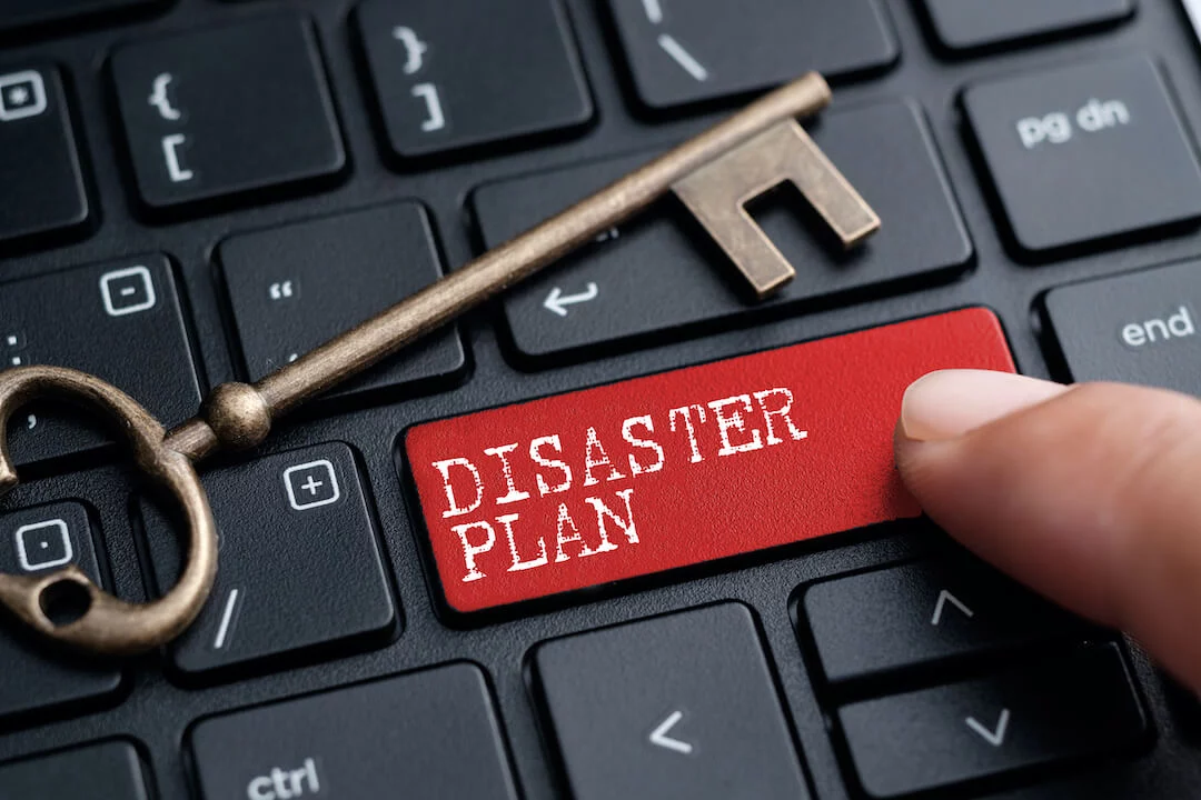 Finger pressing disaster plan button on keyboard with gold key resting on keyboard