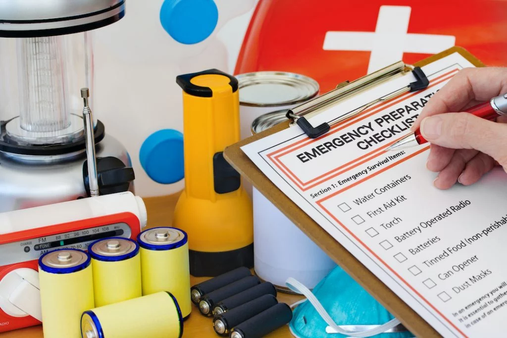 Person reviewing emergency preparedness checklist and looking at batteries, flashlight and first aid kit