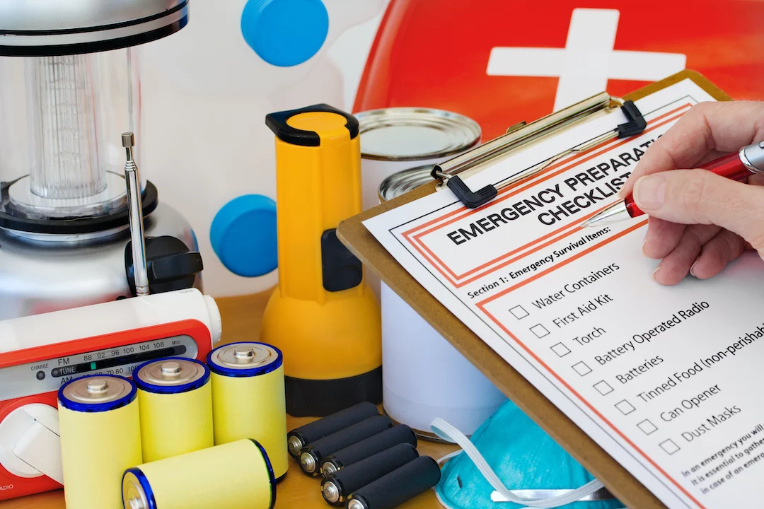 Person reviewing emergency preparedness checklist and looking at batteries, flashlight and first aid kit