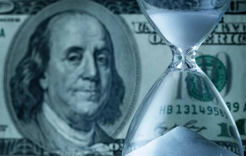 US 100 dollar bill in the background, hourglass in foreground