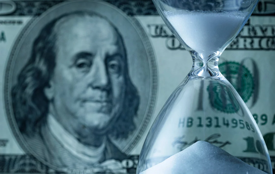 US 100 dollar bill in the background, hourglass in foreground