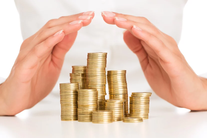 Two female hands protecting a stack of gold coins