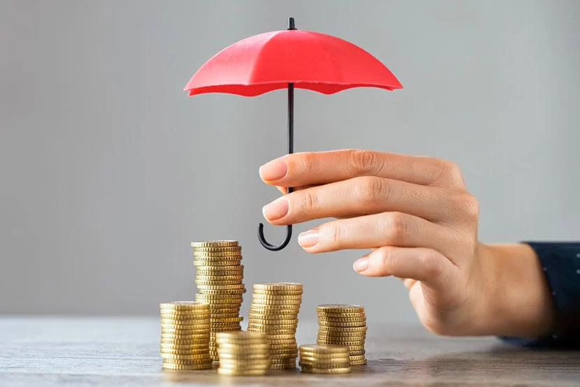 Hand holding umbrella over multiple stacks of gold coins