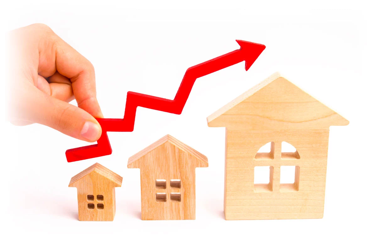 Hand holding upwards red arrow over wooden cutouts of houses