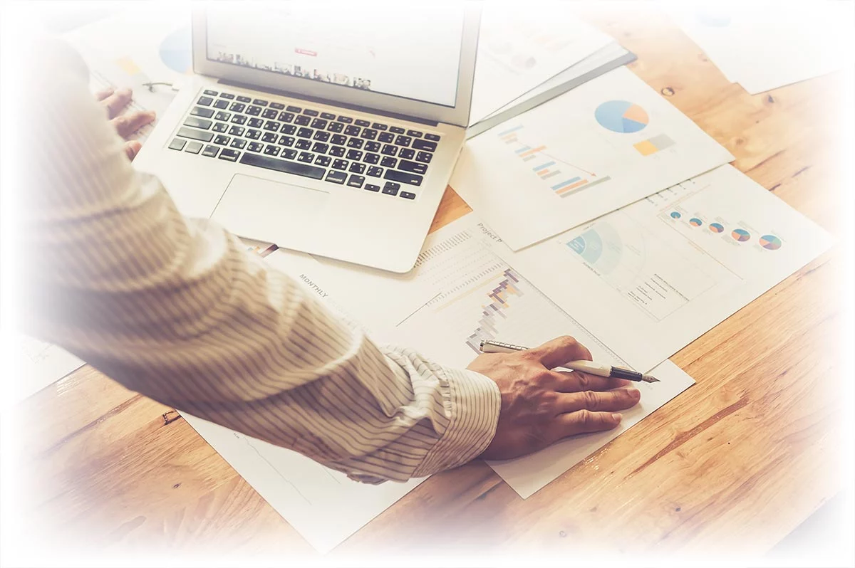 Man looking at laptop and table covered with financial documents.