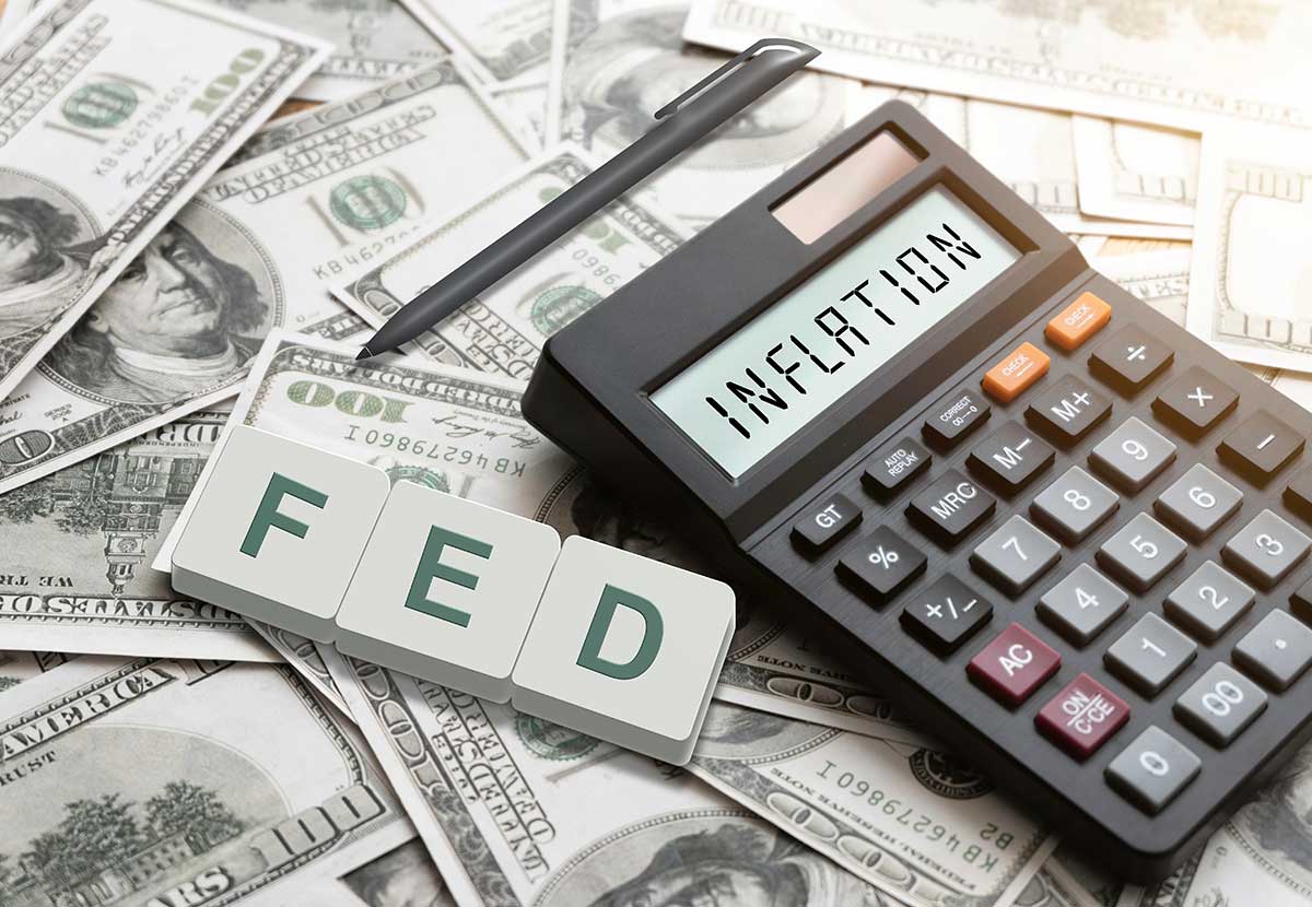 Calculator reading "INFLATION" and word blocks spelling "FED" on pile of $100 notes
