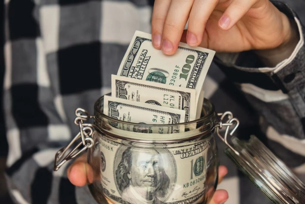 Hand pulling $100 notes from jar