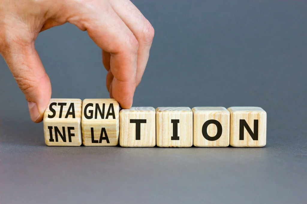 Hand turning letter blocks between "INFLATION" and "STAGNATION"