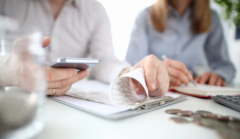 Hands going over receipts with cell phone and notepad