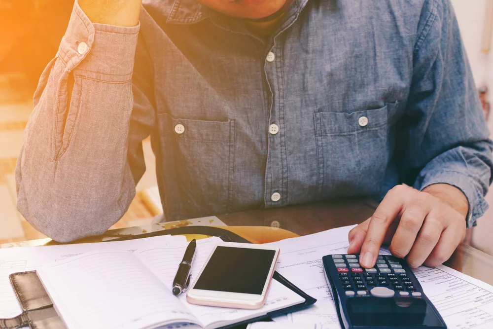 A person in a blue button down shirt using a calculator to pay bills