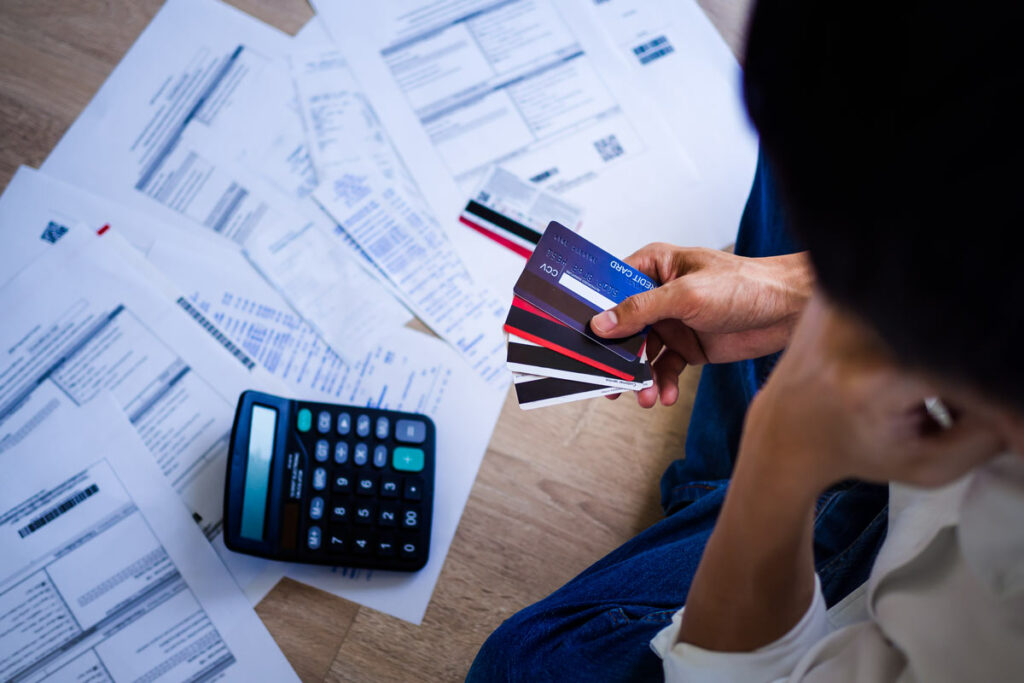 Person looking at bills and calculator while holding credit cards