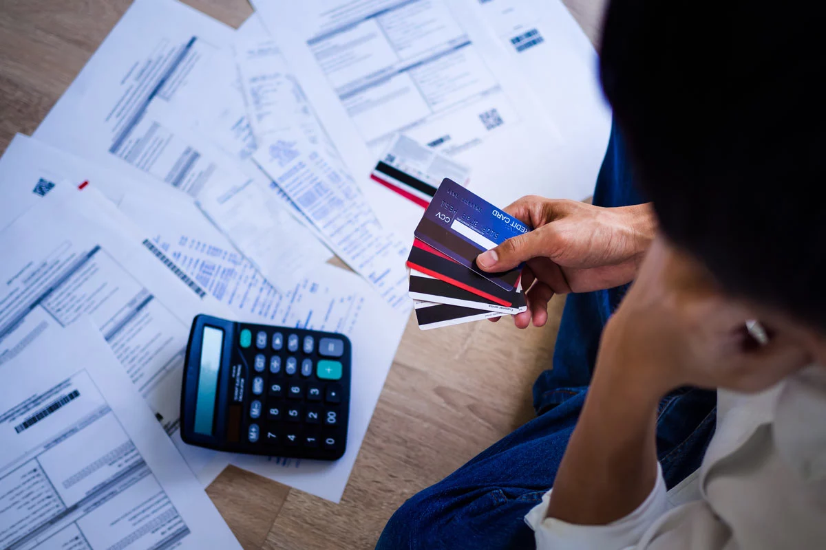 Person looking at bills and calculator while holding credit cards