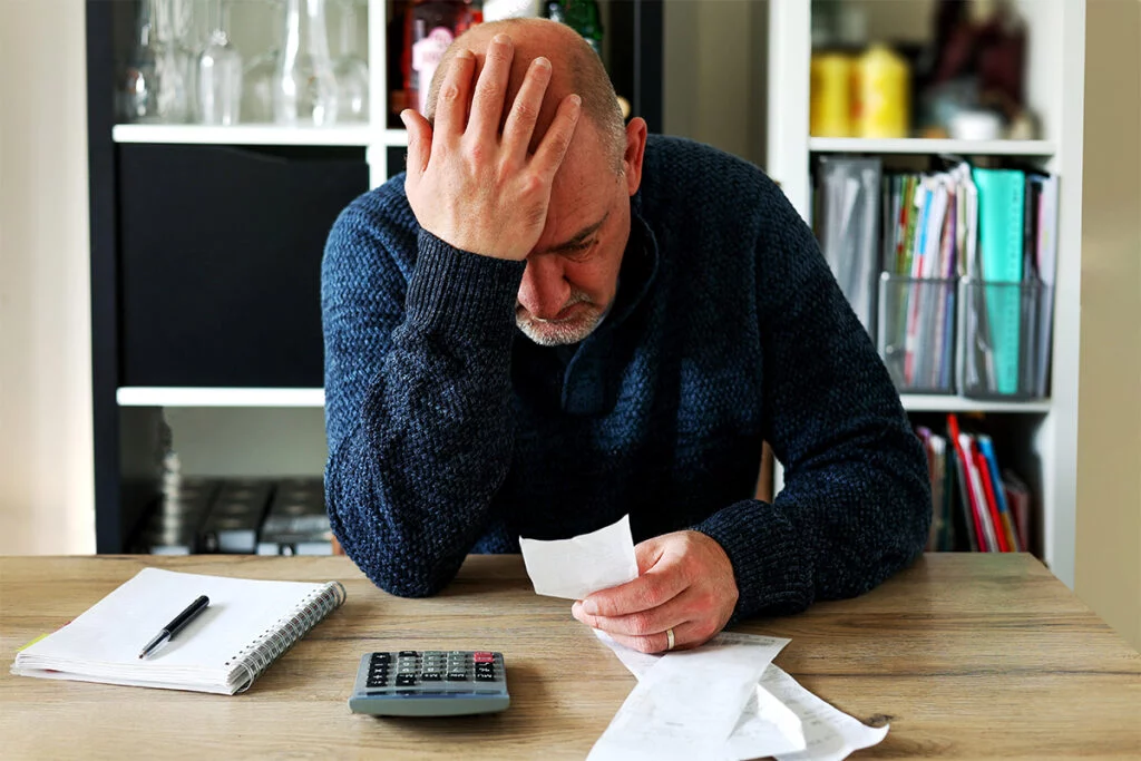 Upset man looking at receipts with calculator