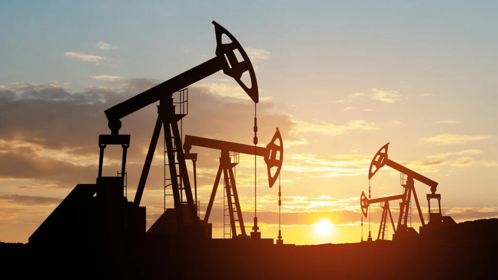 Oil derricks silhouetted against sunset sky