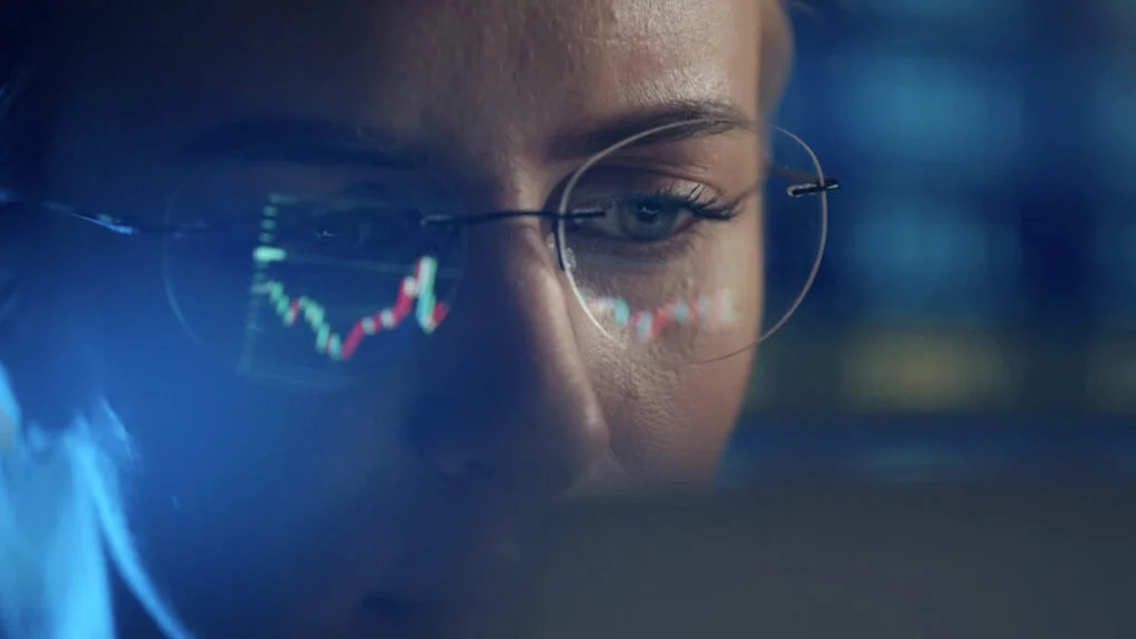 Woman looking at computer screen with chart reflection in her glasses.